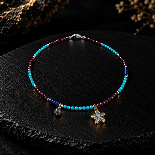 Starfall · 星坠 — iron meteorite five-pointed star in a gold bezel with a round sky-iron bead, on garnet-red and vivid blue stone beads, on black slate